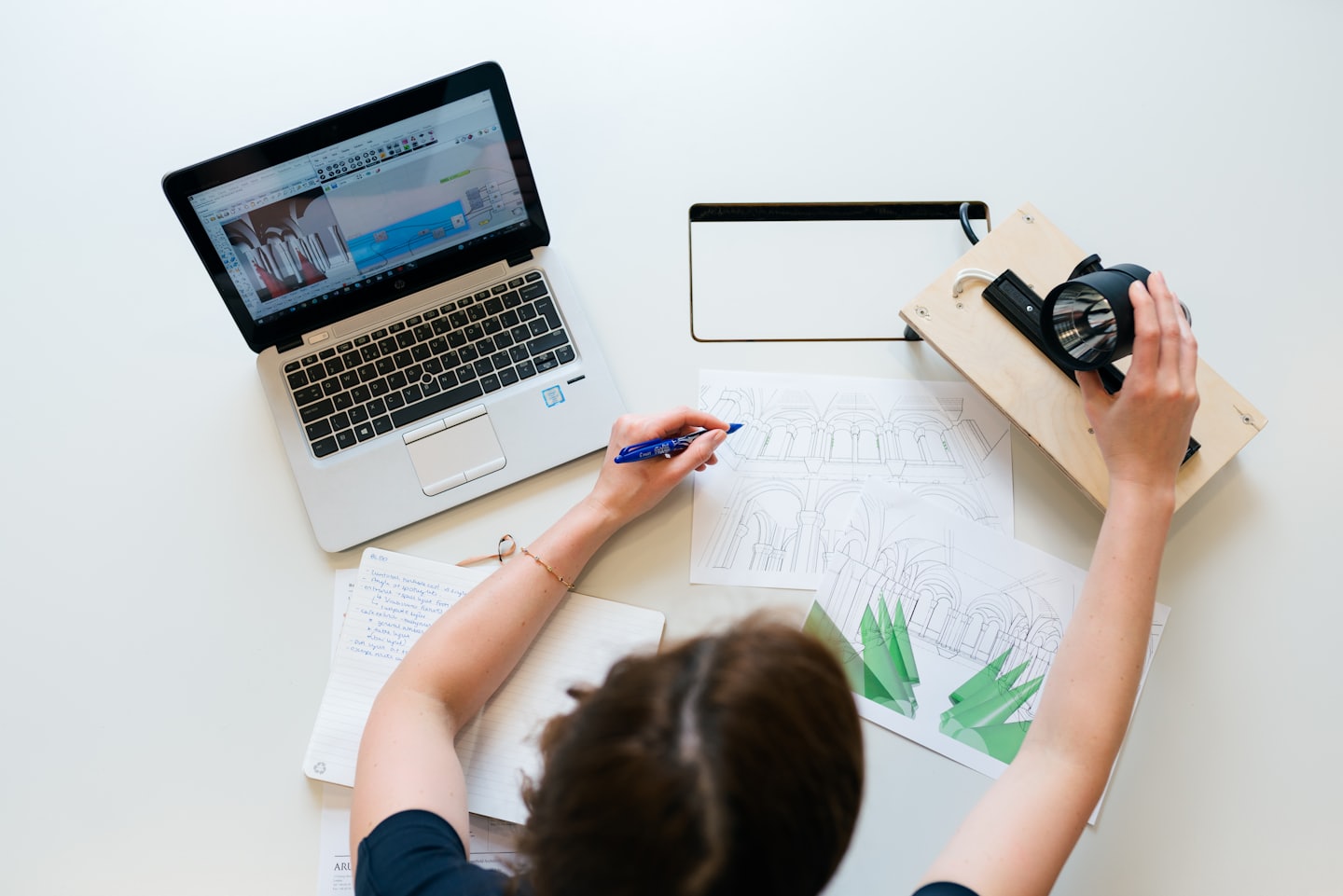 Ein Designer skizziert Gebäudepläne neben einem Laptop und Notizbuch.